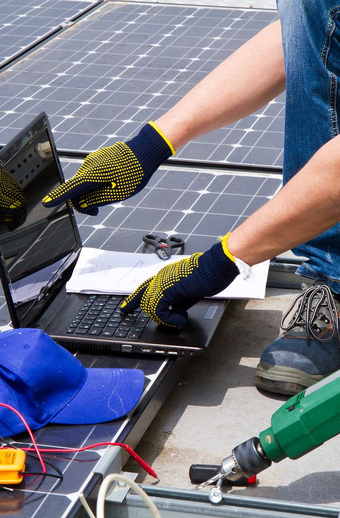 Ein Techniker mit Handschuhen zeigt auf einen Laptop auf einem Solarmodul, während er Werkzeuge und Ausrüstung für Installations- oder Wartungsarbeiten verwendet.